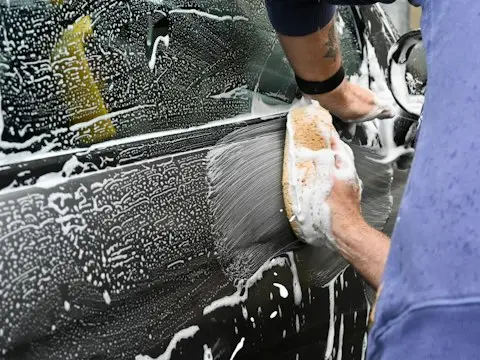 um homem lavando um carro com uma esponja